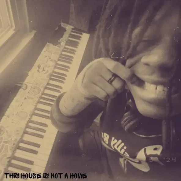 A person smiling and wearing headphones, holding their hand near their face, with a piano in the background and the text "This house is not a home" at the bottom.