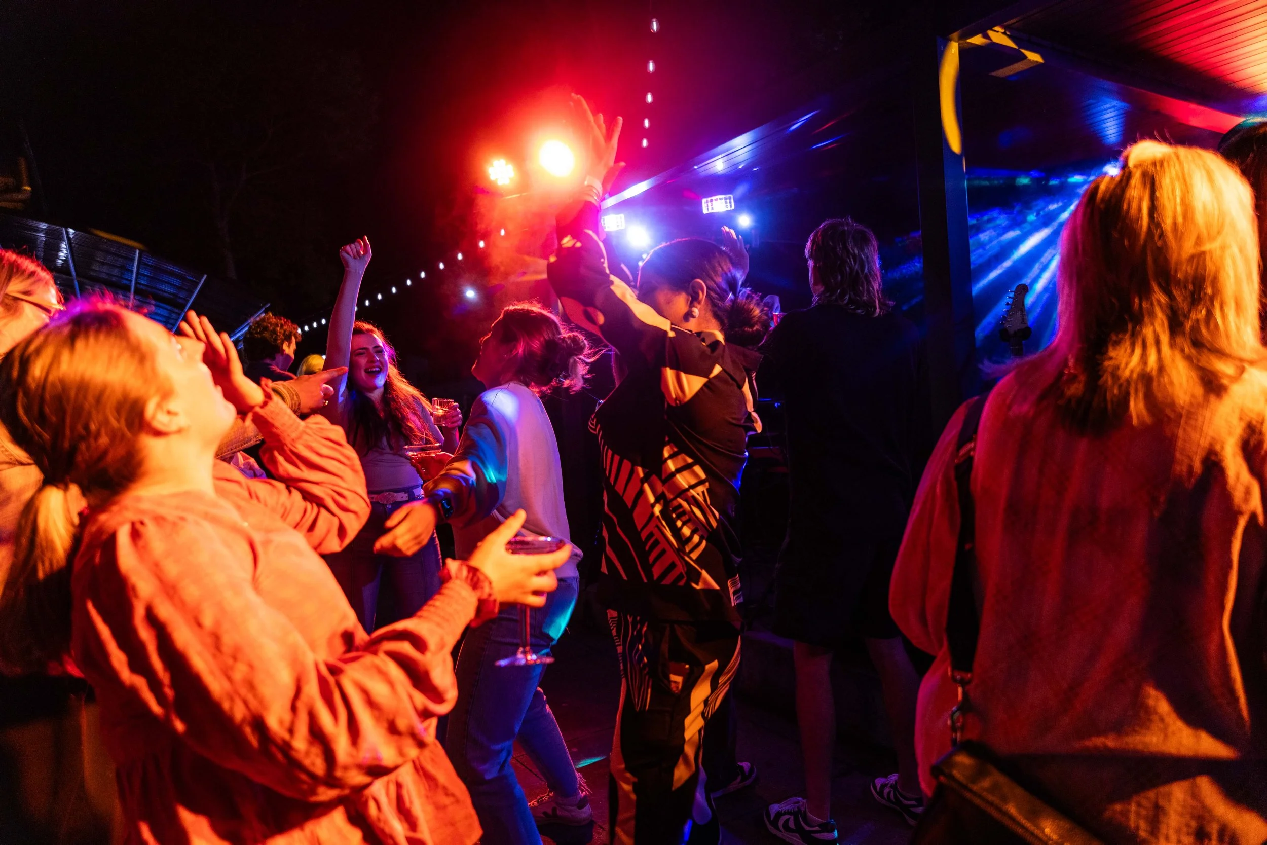 People dancing and enjoying themselves at a nightclub with colorful lights and laser effects.