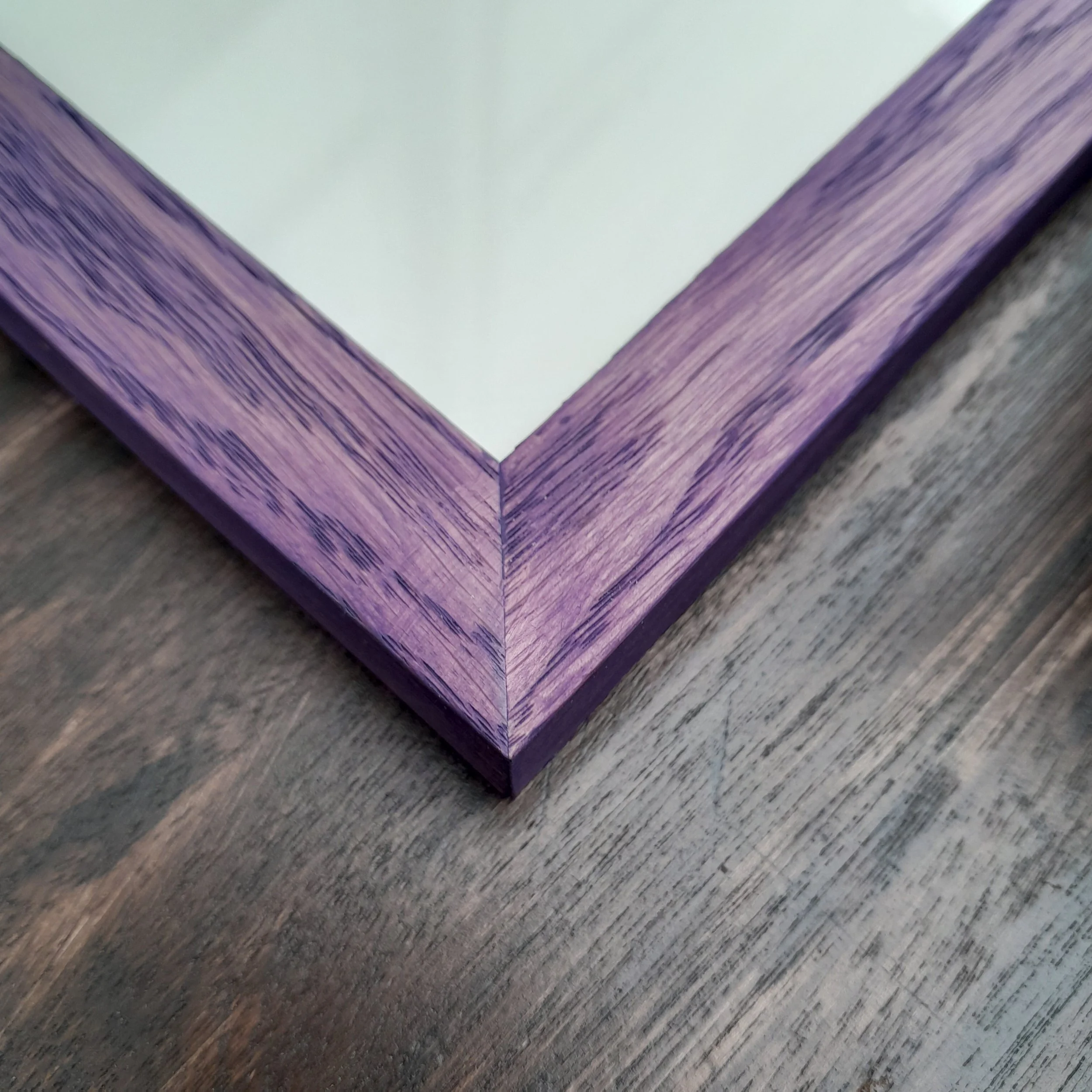 Close-up of a wooden picture frame with purple finish, placed on a wooden surface.
