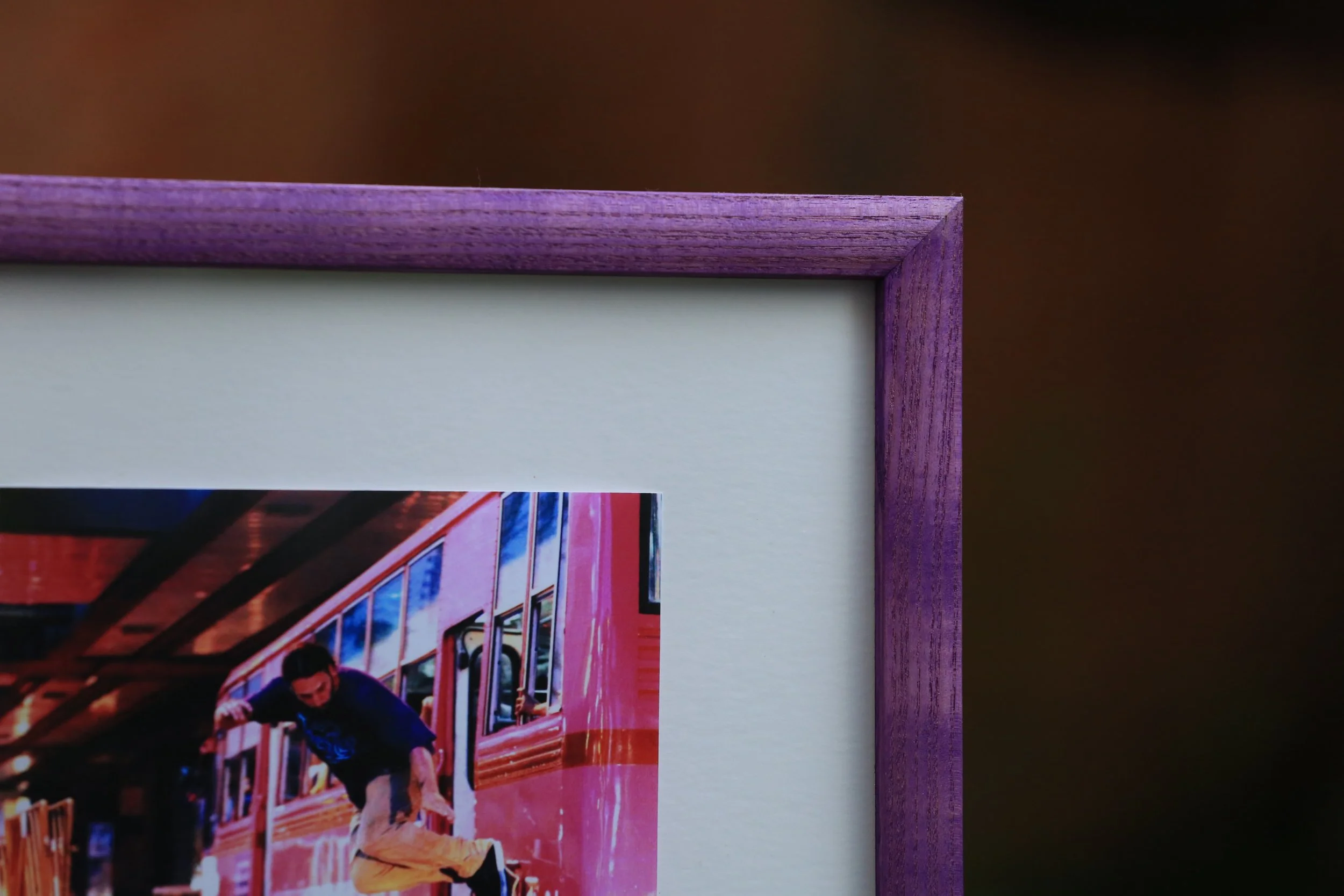 Close-up of a purple wooden picture frame with a photo of a person jumping in front of a red train inside.