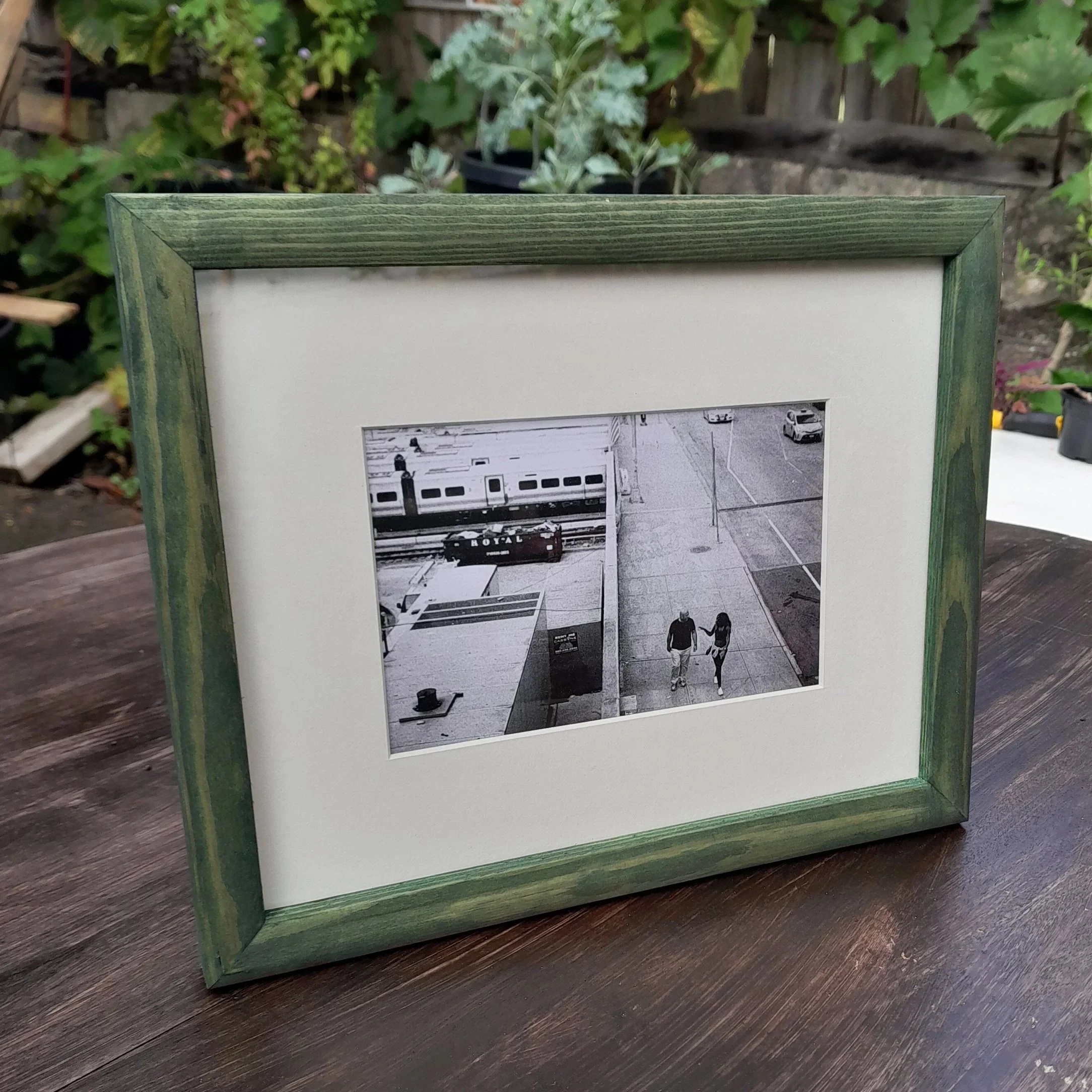 A framed black-and-white photo of a man and woman walking hand in hand on a city sidewalk, with a train passing in the background.