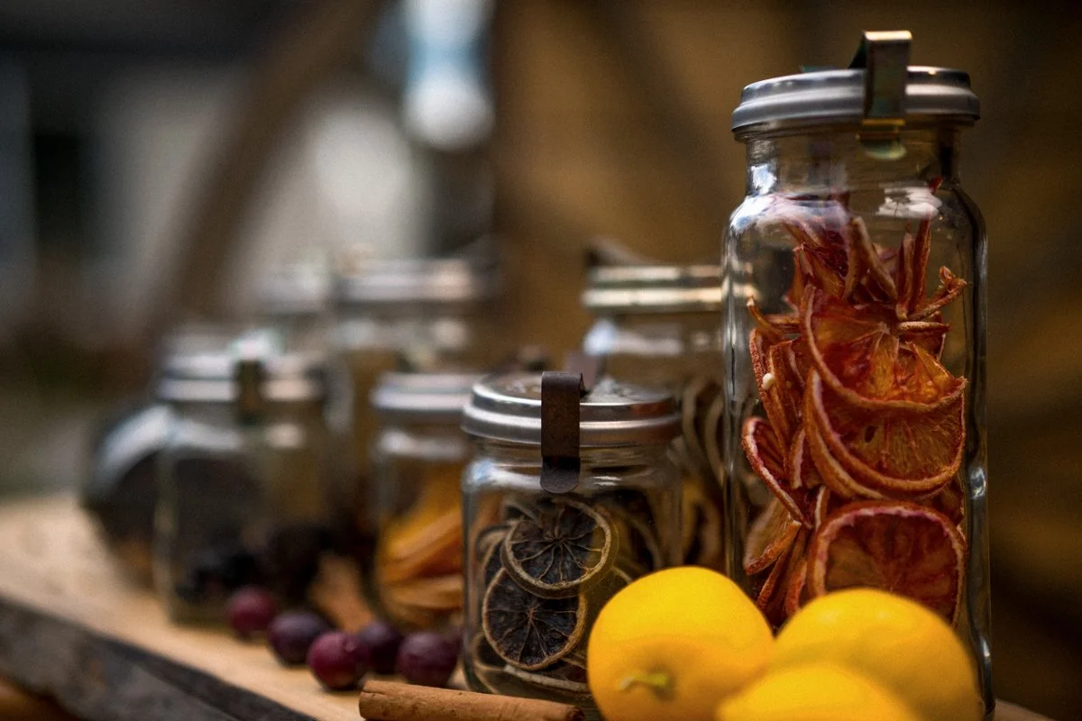 Glass jars filled with dried citrus slices, apples, and other dried fruits on a wooden surface.