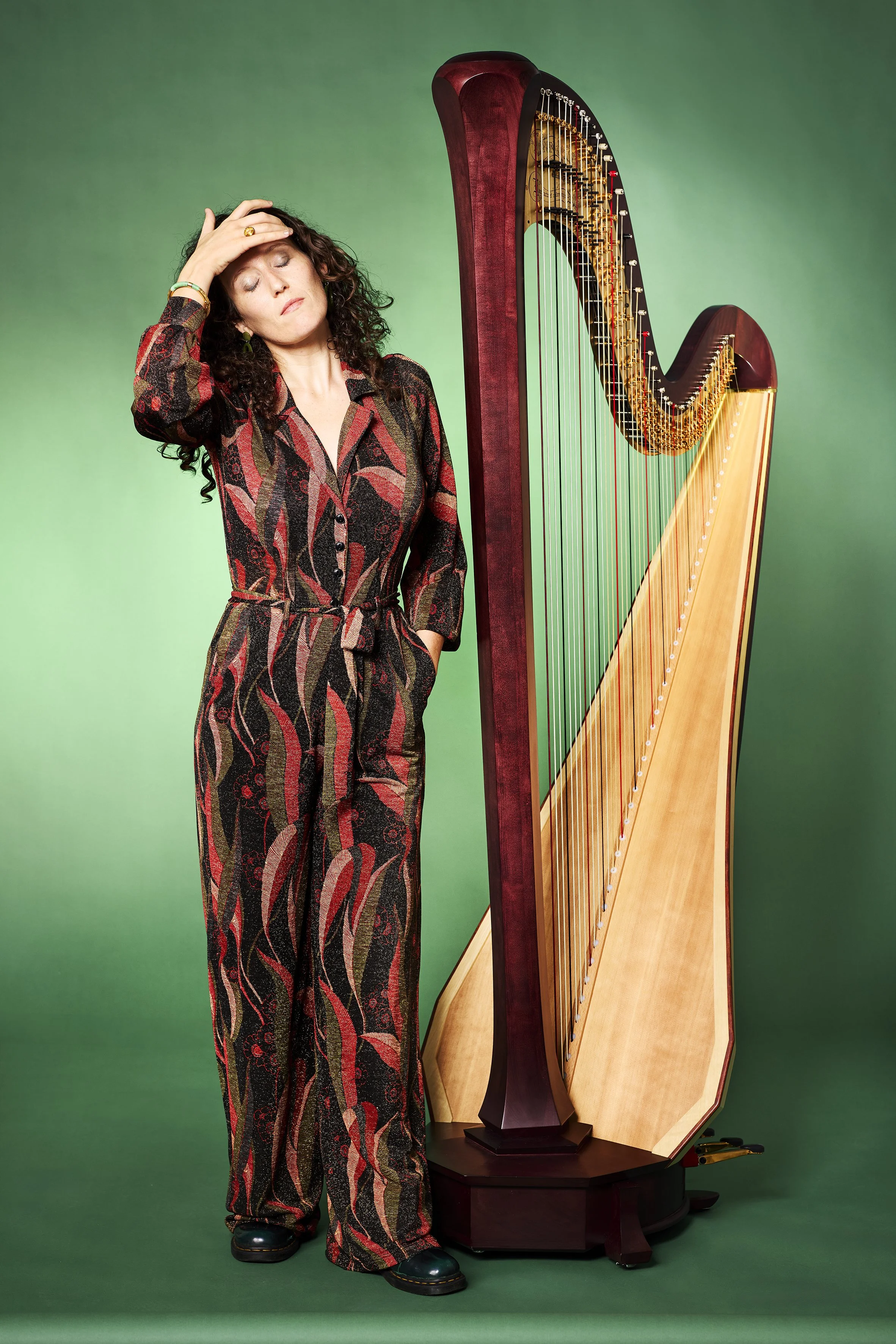 Louisic Dulbecco standing beside a concert harp, green studio background, composed pose