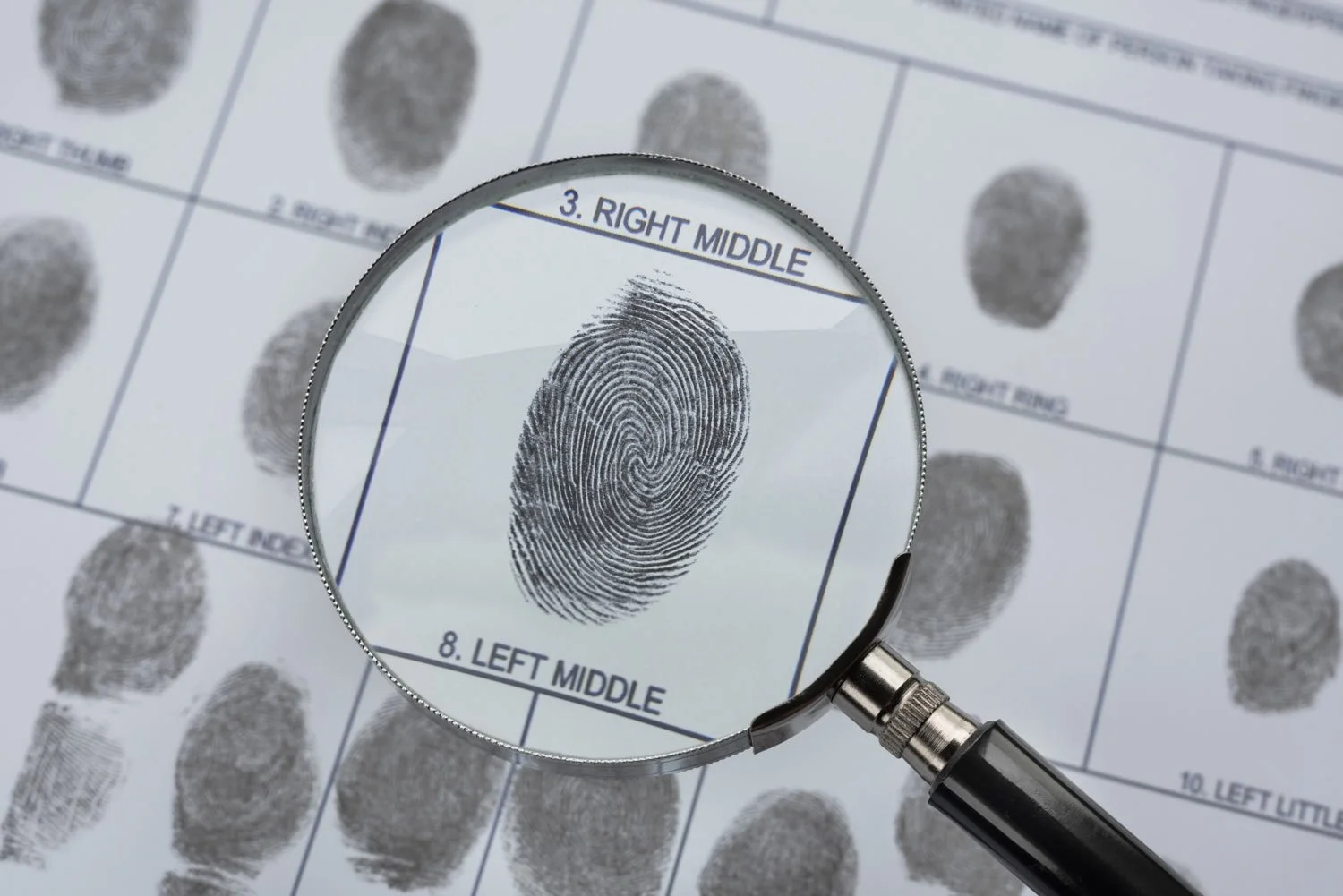 Magnifying glass focusing on a fingerprint on a sheet of paper with ink fingerprint samples and labels for different fingers for ink fingerprinting service Perth Karratha.