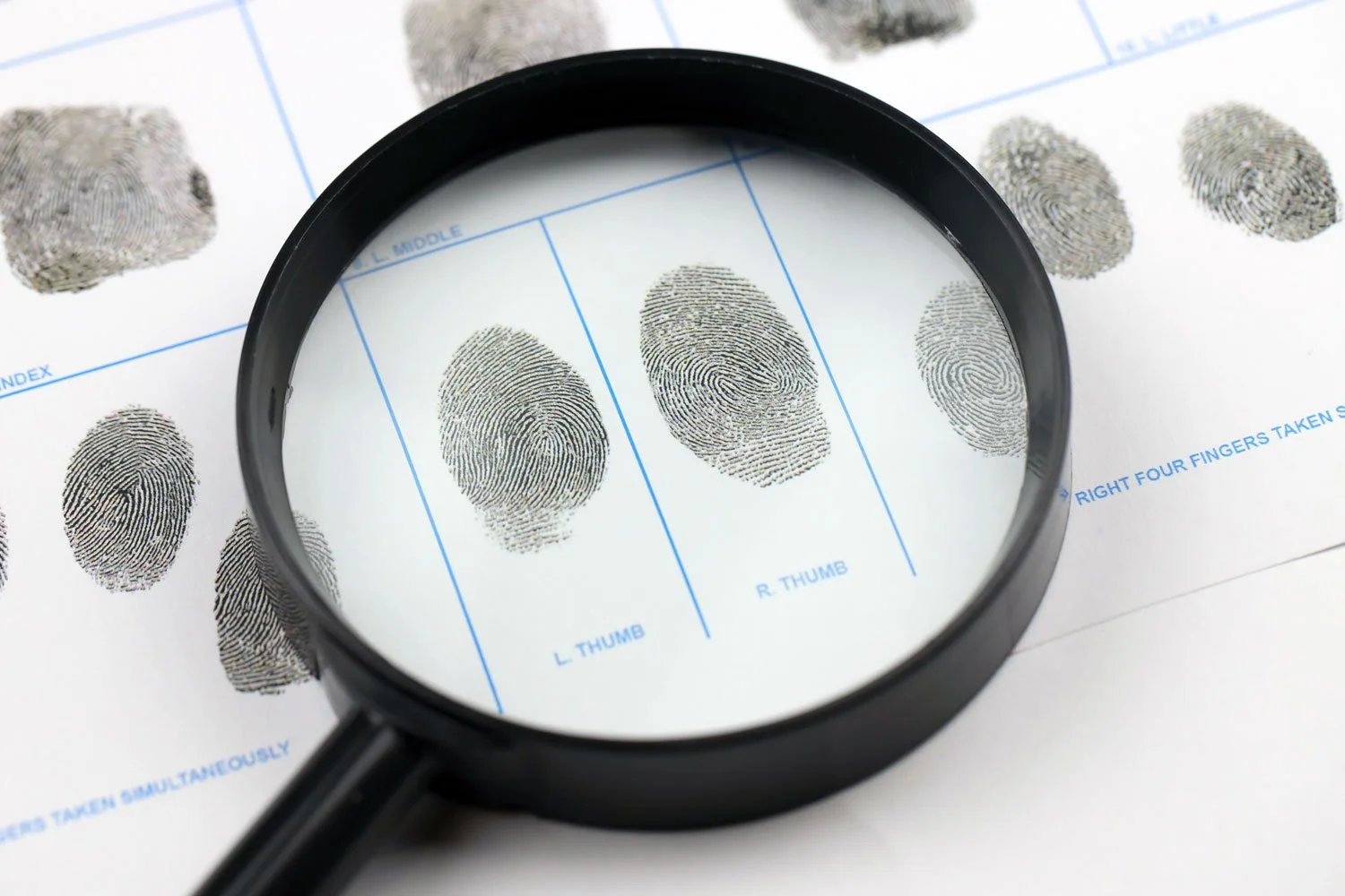 Fingerprint chart viewed through a magnifying glass, showing detailed ink fingerprint patterns for different fingers.