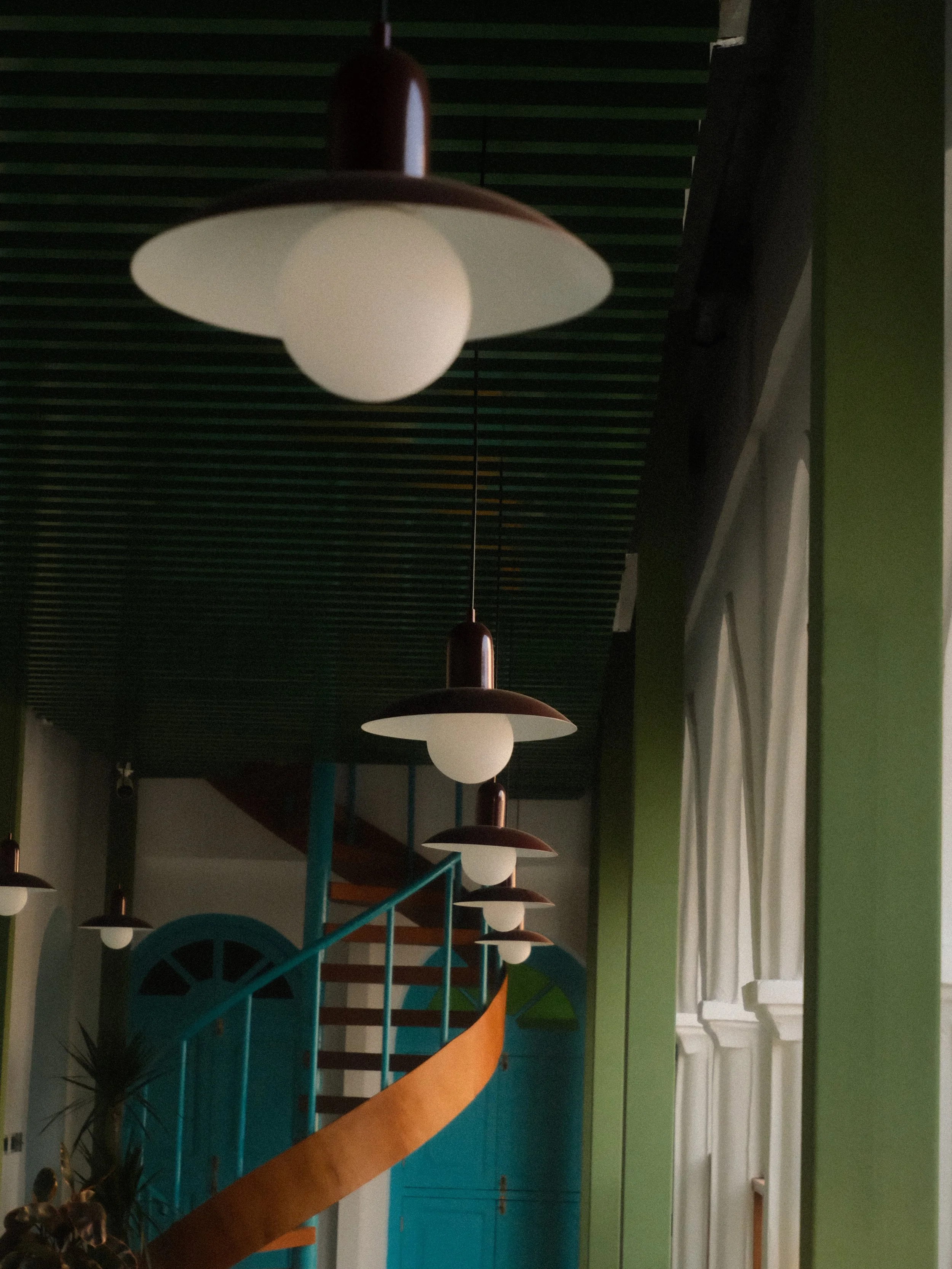 Interior of a colorful room with hanging ceiling lights, a bright spiral staircase, and a turquoise wall with a window.