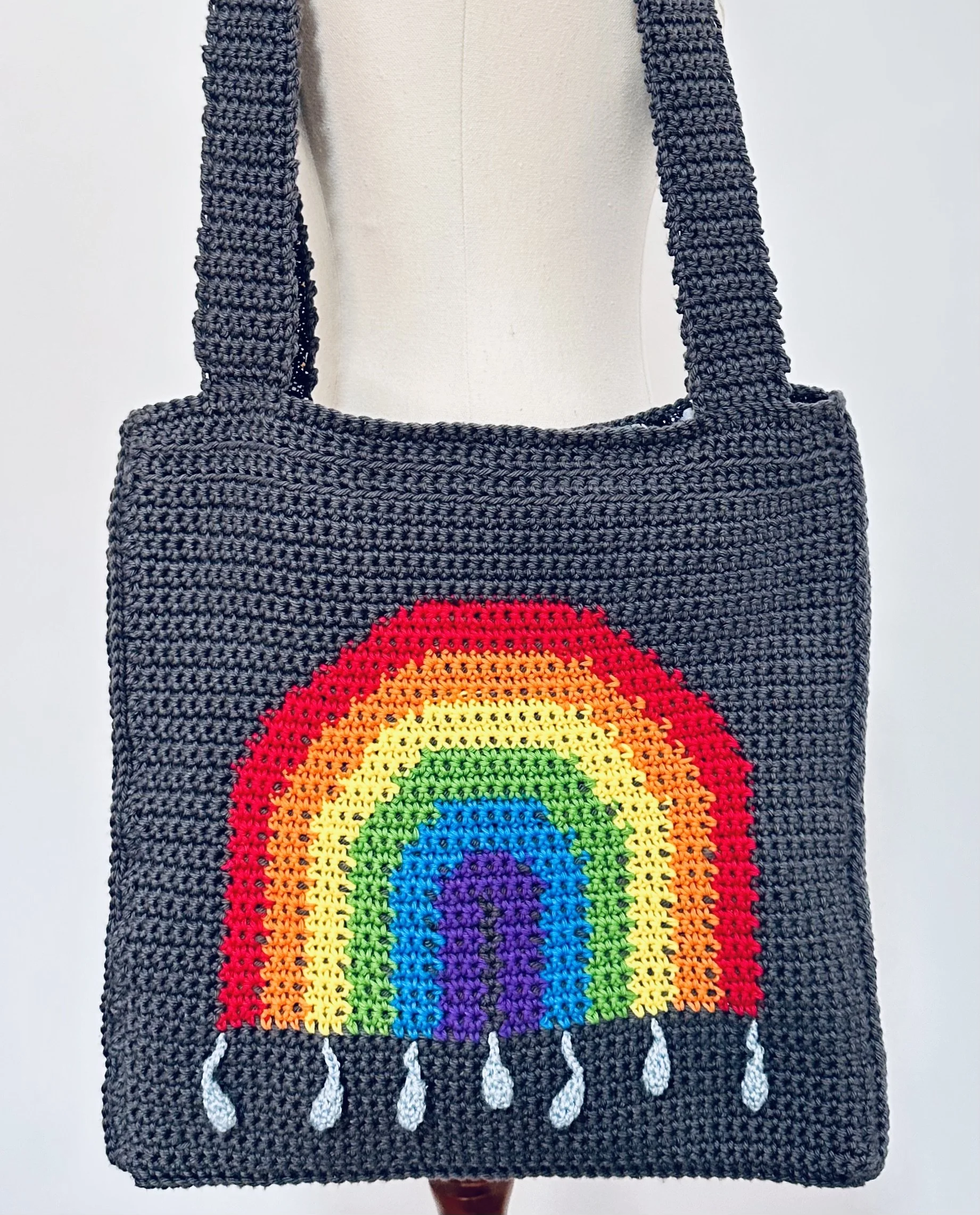 Handmadedark grey crochet tote bag with a colourful rainbow pattern and raindrops at the bottom.