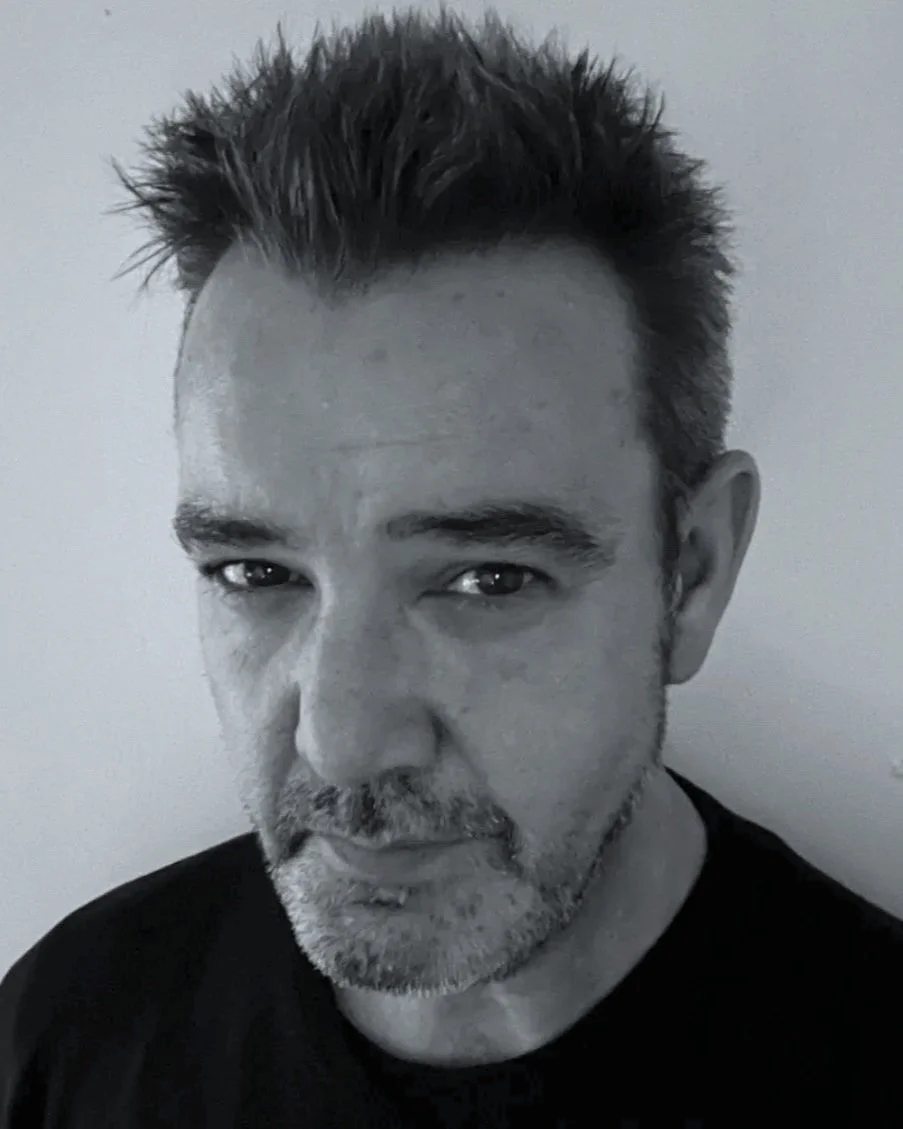 Close-up black-and-white photo of a Editor Steve from Early Morning Edits with spiked hair and a beard looking directly at the camera against a plain background.