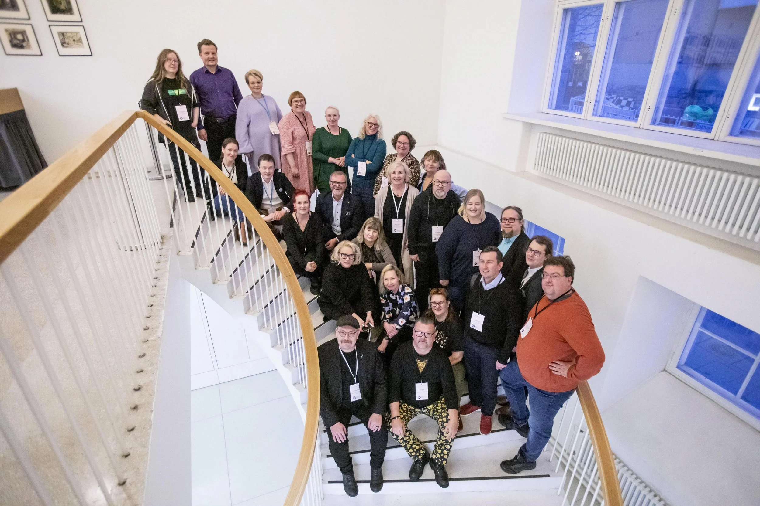 Ihmisiä asettuneena kiertävään portaikkoon poseeraamassa ylhäältä päin katsottuna.