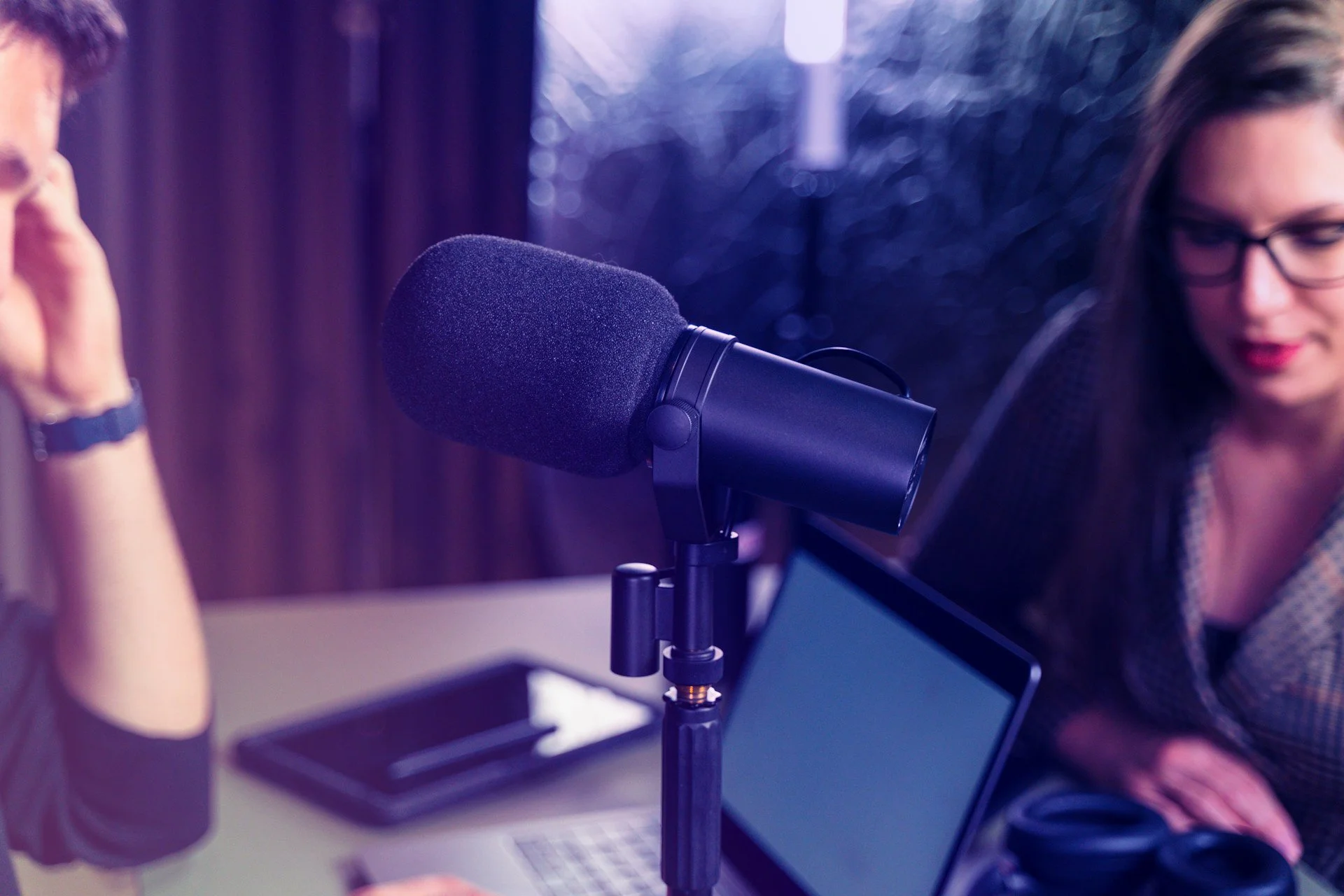 Podcast-studio: mikrofoni, laptop ja kaksi naista keskustelemassa.