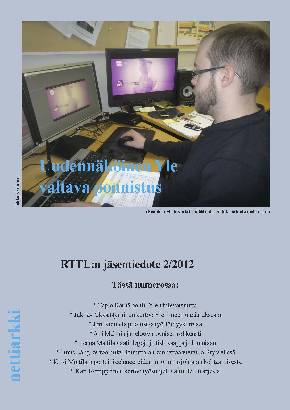 "Liiton Arkki" kansilehti, jossa työskentelee mies tietokoneen ääressä, kaksi monitoria ja työpöydällä papereita ja puhelimia.