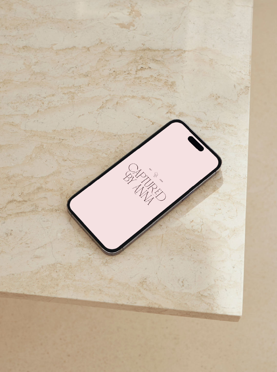 Smartphone on a light-coloured marble surface displaying logo branding design for Captured by Anna on the Sunshine Coast on a pale pink background.