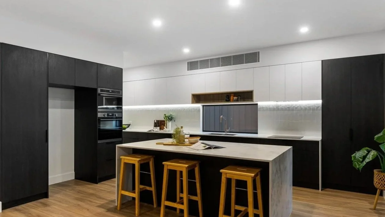 Modern kitchen with black and white cabinets, a large island with wooden stools, and wooden flooring.