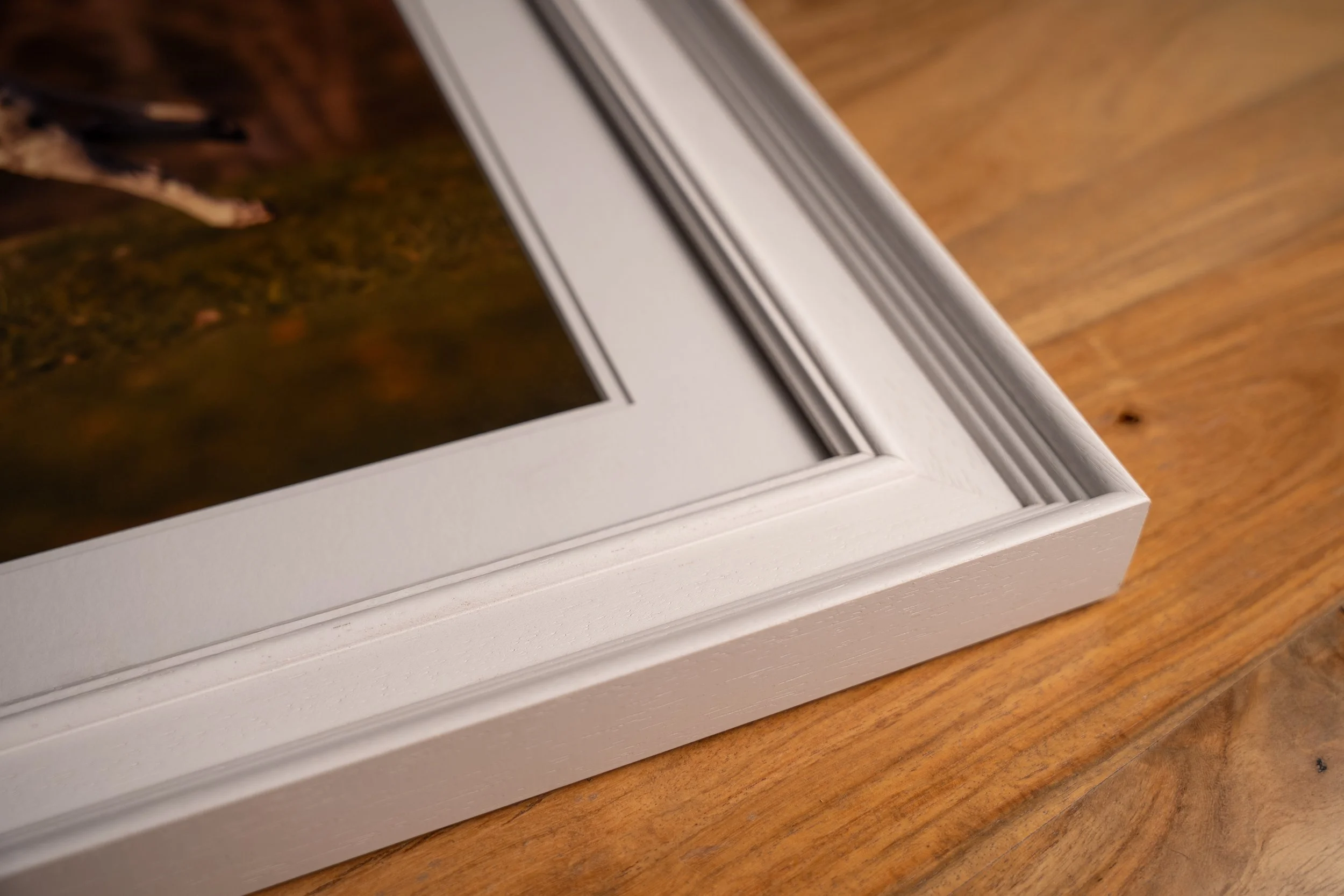 Close-up of a white picture frame with decorative molding, resting on a wooden surface.