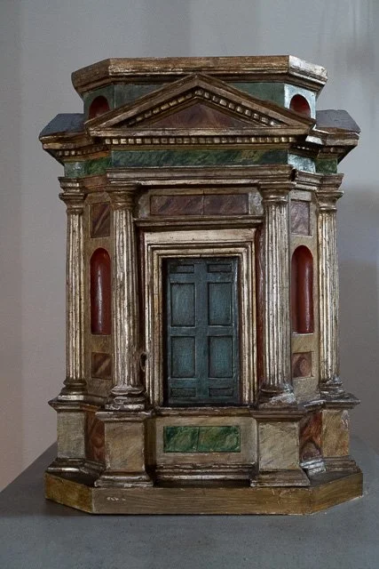 A miniature model of a classical building facade with columns, a triangular pediment, and a closed door.