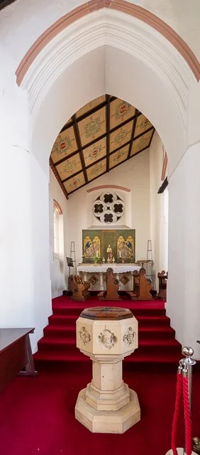 Interior of a church with red carpeted stairs leading to an altar, featuring religious icons and a decorative ceiling.