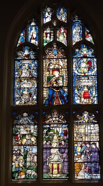 Colorful stained glass church window with religious scenes, including angels, saints, and biblical figures.