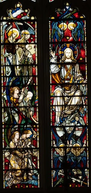 Colorful stained glass windows depicting religious scenes and figures, including angels and saints, in a church setting.