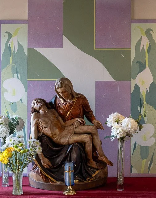 Close-up of a religious sculpture depicting Jesus Christ's lifeless body being held by a woman, with flowers and a candle placed around it.