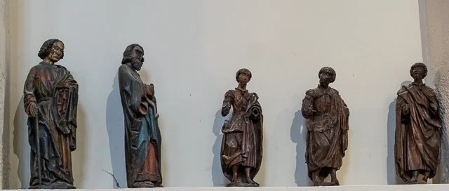 Six wooden statues of people displayed on a wall, each with different clothing and poses.