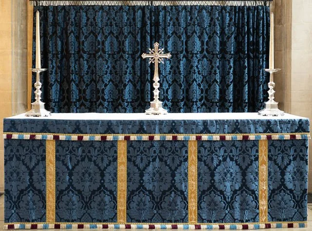A church altar covered with a blue cloth and decorated with a cross and two silver candlesticks.