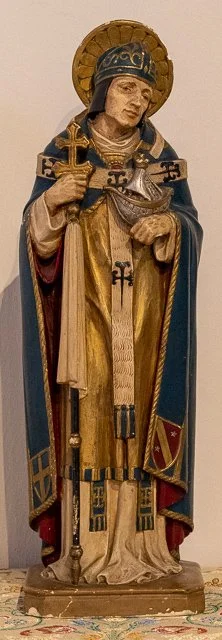 Wooden statue of a saint dressed in medieval armor, holding a sword and a cross, with a golden halo behind the head.