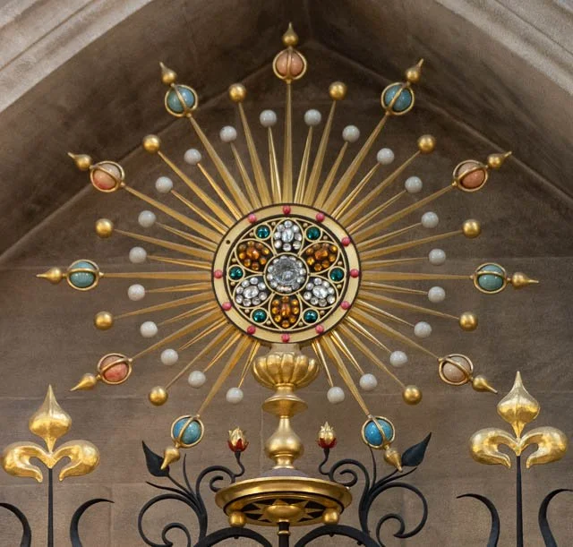 Ornate religious monstrance with colorful gemstones and gold accents, displayed inside a church.
