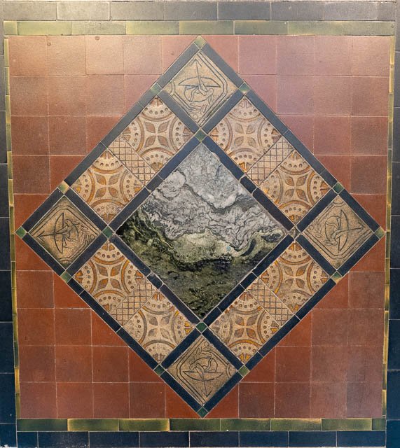 Decorative tile mural featuring a central abstract pattern surrounded by geometric patterns and bordered by reddish-brown tiles.
