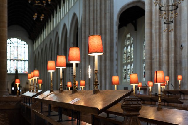 Rows of wooden lecterns with orange lamps in a historic church with stained glass windows.