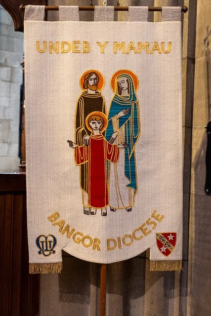 A fabric banner featuring an embroidered depiction of three religious figures, with the text "Undeb Y Mamau" at the top and "Bangor Diocesan" at the bottom, along with two embroidered crests.