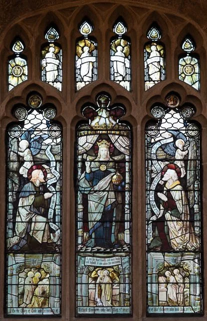 Colorful stained glass church window depicting religious figures, angels, and saints in a traditional style.