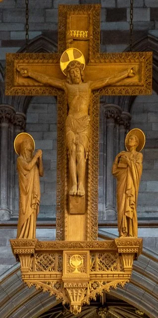 Wooden crucifix with Jesus Christ on the cross flanked by two saints or apostles, inside a church.