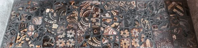 Close-up of a decorative tile surface with floral and geometric patterns in blue, tan, and white colors.