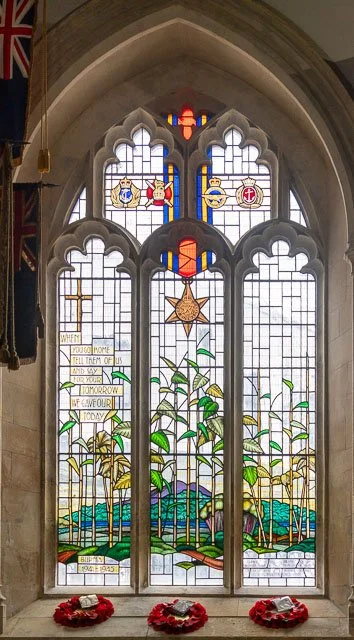 Stained glass window with a star, plants, and tiny flags, with red wreaths at the bottom.
