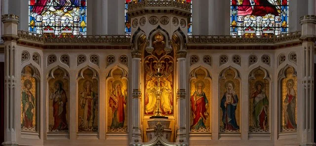 Interior of a church with stained glass windows and religious icons on the altar wall.