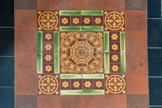 Decorative ceramic tile pattern on the floor with a central floral design, surrounded by smaller floral accents and green striped borders.