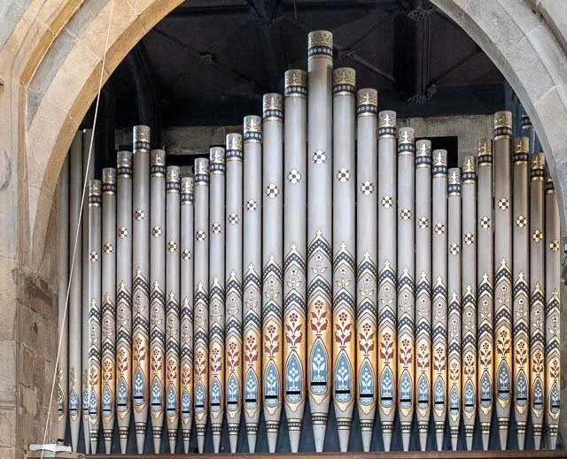Large pipe organ with painted decorative designs inside a stone building.