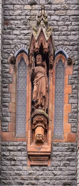 A stone church wall with gothic-style stained glass windows and a detailed religious sculpture