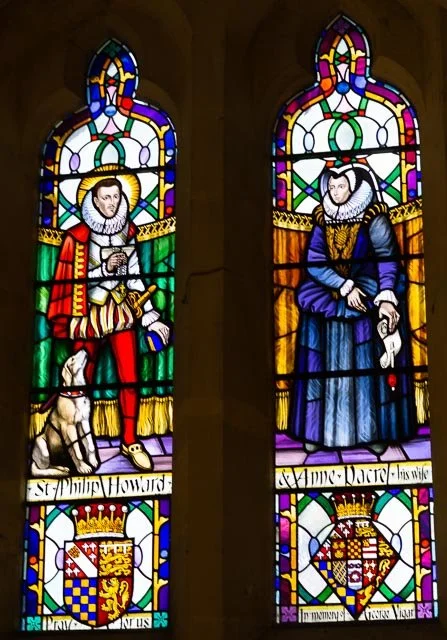 Colorful stained glass windows depicting King Philip Howard on the left, and Queen Elizabeth on the right, each with a heraldic shield at the bottom.