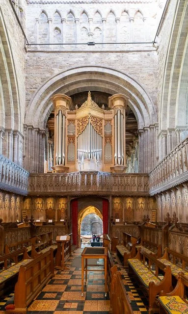 Interior of a church or cathedral with an ornate pipe organ at the front, wooden pews, and intricate woodwork along the walls.