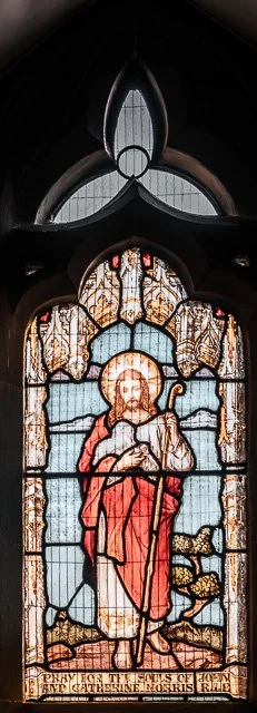Stained glass window depicting Jesus Christ holding a staff, with a dove, lamb, and clouds, representing Christian themes.