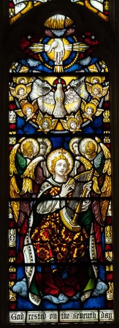 Stained glass window depicting angels, a dove, and religious figures with a harp and banner, symbolizing a biblical scene.