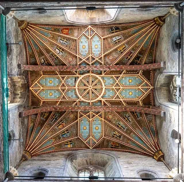Interior view of a decorated cathedral ceiling with intricate wooden beams and painted artwork, seen from below.