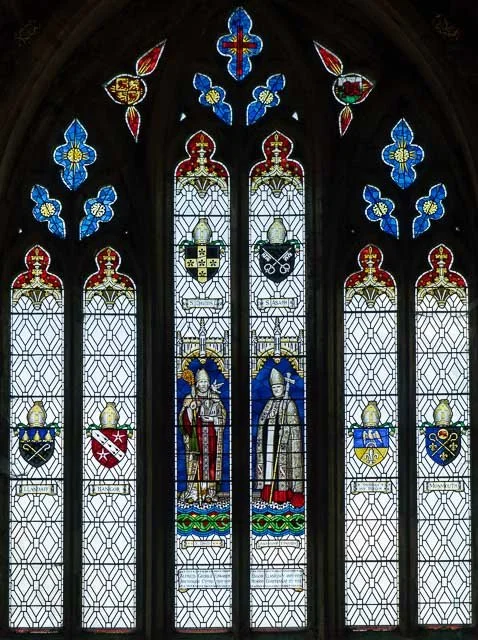 Colorful stained glass window with medieval coats of arms and figures in robes.