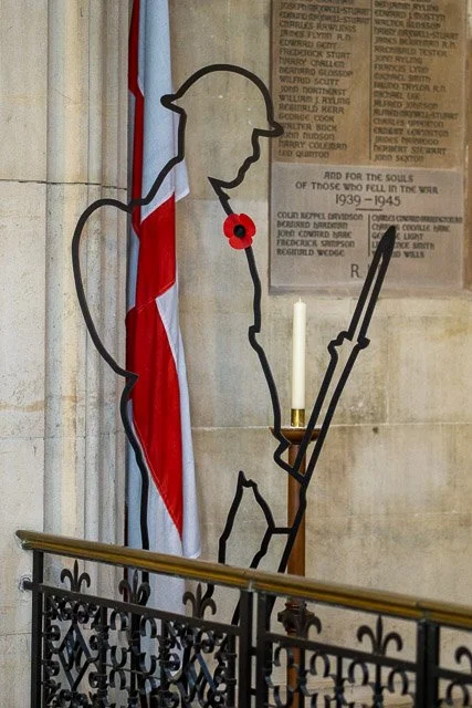 Outline of a soldier with a poppy, standing next to a British flag and a memorial plaque.