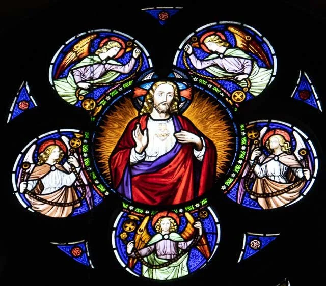 Stained glass window depicting Jesus Christ surrounded by angels and saints.