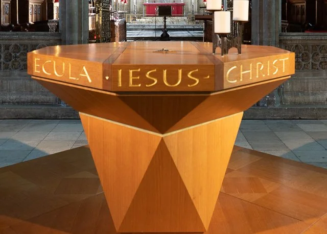 A wooden altar in a church with the words 'EULA IESUS CHRIST' engraved on it, surrounded by candles and church architecture.