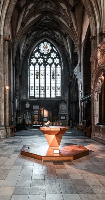 Inside a Gothic cathedral with high arched ceilings, stained glass windows, and a modern pulpit in the center.