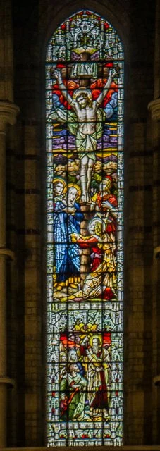 A tall stained glass window depicting the crucifixion of Jesus Christ, with Jesus on the cross surrounded by figures including Mary and John.