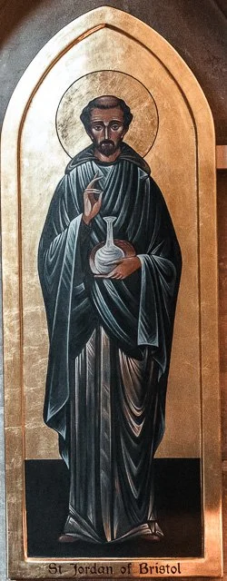 Painting of St. Jordan of Bristol, depicted as a bearded man with a halo, holding a flask and a pipette, dressed in dark robes, on a gold background with an arched frame.